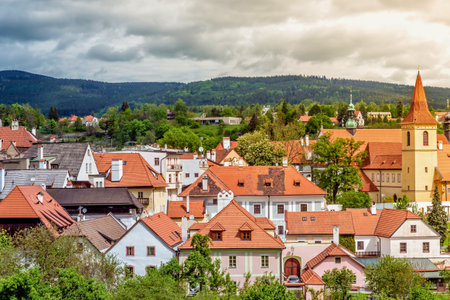 A picturesque view of a historic European town featuring many red tiled roofs, nestled against a backdrop of lush green hills and a cloudy sky.の写真素材