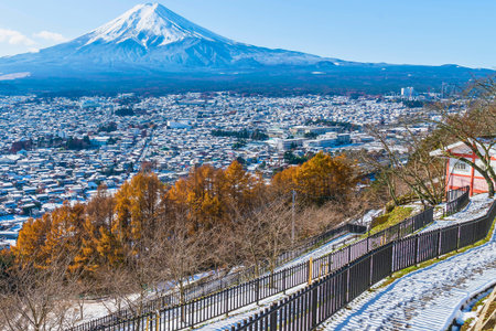 A breathtaking view of Mount Fuji towering over a snow-covered town, with vibrant autumn foliage in the foreground.の写真素材