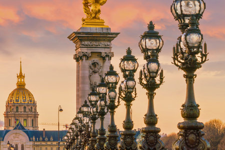 Close-up of decorative lampposts on a bridge in Paris, with the golden dome of a building visible in the soft, warm light of sunset.の写真素材