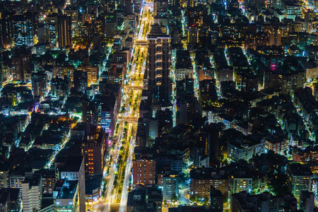 An abstract, high-angle perspective of a city at night, showcasing a central illuminated street with surrounding buildings and lights.の写真素材