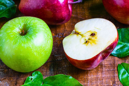 A vibrant assortment of fresh green and red apples, one halved, surrounded by bright green spinach leaves on a rustic wooden background.の写真素材