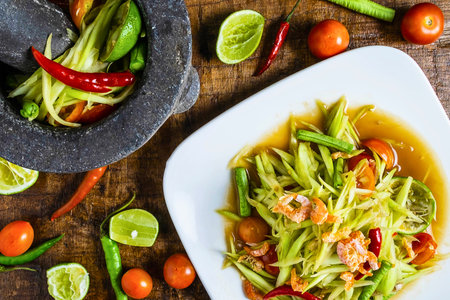 A vibrant and spicy green papaya salad served with fresh ingredients and a mortar and pestle, showcasing authentic Thai cuisine.の写真素材