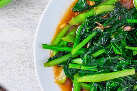 A close-up of vibrant green leafy vegetables, likely spinach or bok choy, stir-fried in a glossy savory sauce, served on a white plate.の写真素材