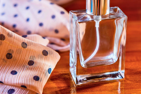 A clear glass perfume bottle with a silver cap sits beside a soft, patterned fabric, bathed in warm, inviting light.の写真素材