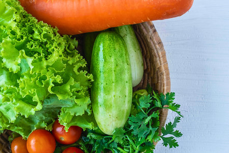 A close-up overhead view of a basket filled with vibrant, fresh vegetables like a carrot, cucumber, lettuce, tomatoes, and parsley.の写真素材
