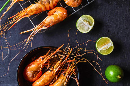 Grilled prawns are presented with halved limes and a whole lime, showcasing a fresh and appetizing seafood dish.の写真素材