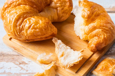 Close-up of flaky, golden brown croissants on a wooden cutting board, one broken open revealing its airy interior.の写真素材