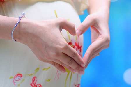 A close-up shot of hands creating a heart shape over a pregnant woman's belly, symbolizing love and anticipation.の写真素材