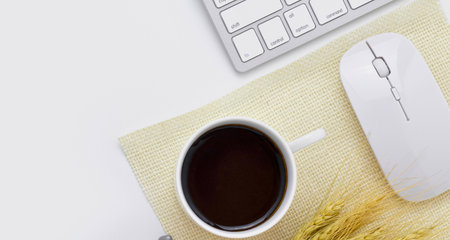 A clean, minimalist workspace featuring a cup of black coffee, a white computer mouse, and a keyboard on a light-colored cloth.の写真素材