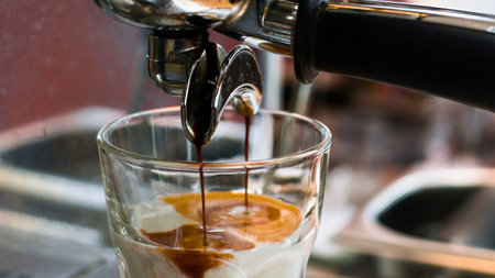 A close-up shot of dark espresso dripping into a clear glass filled with ice and a creamy beverage.の写真素材
