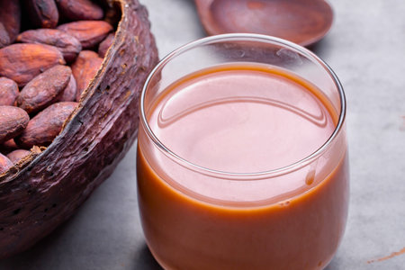 A refreshing chocolate beverage in a glass sits beside a cracked cacao pod filled with beans, hinting at its origin.の写真素材