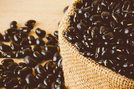 A close-up view of dark roasted coffee beans spilling from a textured burlap sack onto a light...