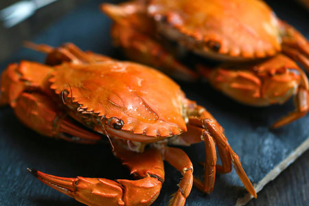 Close-up shot of two bright orange, whole steamed crabs arranged on a dark, textured surface, ready...