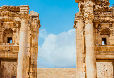 Majestic stone columns and archways of ancient Roman ruins stand against a vibrant blue sky with fluffy white clouds.の写真素材
