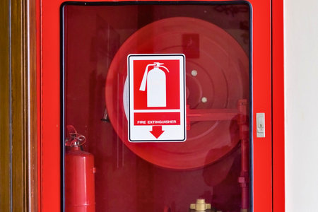 A bright red cabinet encloses a fire extinguisher, coiled hose, and a prominent fire safety sign.の写真素材
