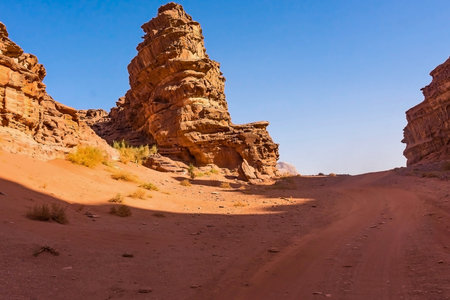 Dramatic, weathered sandstone spires rise from a sandy desert floor, bathed in warm sunlight with a vast blue sky above.の写真素材