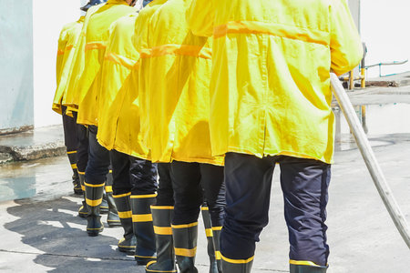A group of people wearing matching yellow raincoats, dark pants, and boots stand in a line, some holding cleaning tools.の写真素材