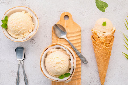 Refreshing coconut ice cream presented in a natural coconut shell and a crispy waffle cone, garnished with mint leaves.の写真素材