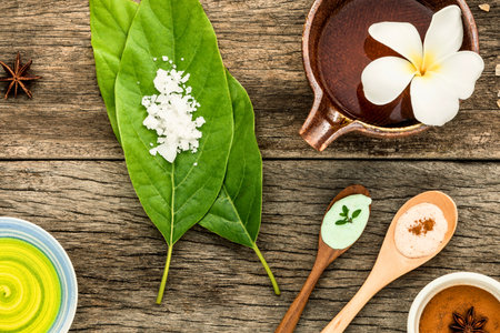 A flat lay of natural ingredients, including green leaves, spices, and liquids, arranged on a rustic wooden surface, suggesting traditional remedies.の写真素材