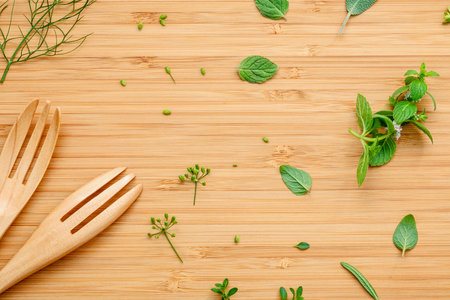 Overhead view of two wooden forks and scattered fresh herbs on a textured bamboo surface, suggesting a culinary theme.の写真素材