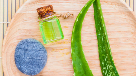 Overhead view of aloe vera leaves, a small bottle of green oil, and a pile of blue clay on a wooden surface.の写真素材
