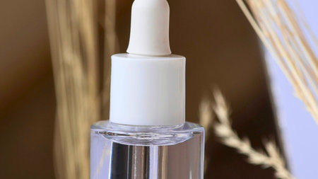 A minimalist shot of a skincare dropper bottle with a white cap and clear serum. Natural elements create a soft, earthy backdrop.の写真素材