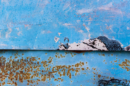 A textured abstract image featuring peeling blue paint, rust patches, and a distant mountain silhouette against a bright sky.の写真素材
