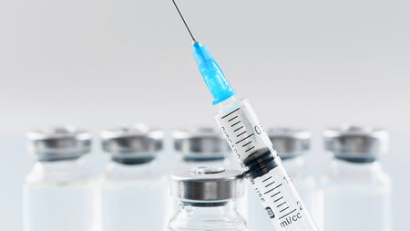 A close-up shot of a medical syringe with a blue tip, poised above several blurred glass vials, suggesting medical treatment or vaccination.の写真素材