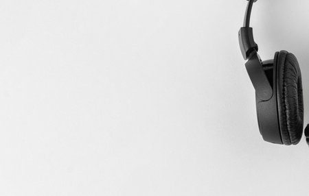 A pair of black over-ear headphones are shown hanging from the right side of the frame against a plain white wall.の写真素材