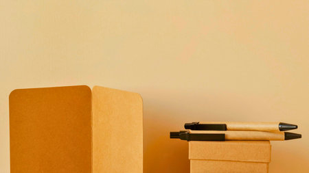 Two pens rest on a small cardboard box, positioned next to a larger, curved wooden object against a plain background.の写真素材