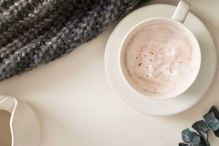A warm cup of coffee sits on a saucer next to a textured blanket and eucalyptus sprigs, evoking a sense of comfort and relaxation.の写真素材