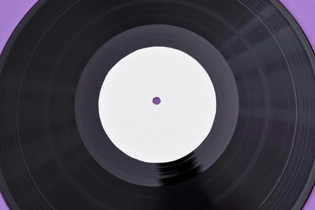 A top-down view of a black vinyl record with a plain white label in the center, against a soft purple background.の写真素材