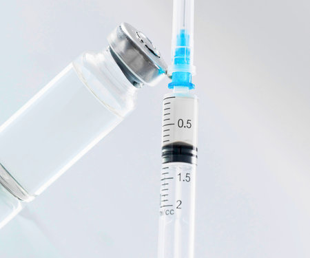 A close-up shot of a medical syringe with a blue tip, positioned next to a glass vial, ready for administering medication.の写真素材