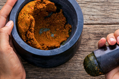 A close-up shot shows hands grinding spices in a stone mortar and pestle, preparing an aromatic paste for cooking.の写真素材