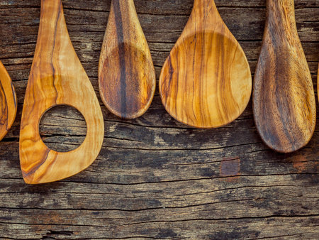 A close-up, top-down view of several handcrafted wooden spoons with varying shapes and textures resting on a rough, aged wooden background.の写真素材