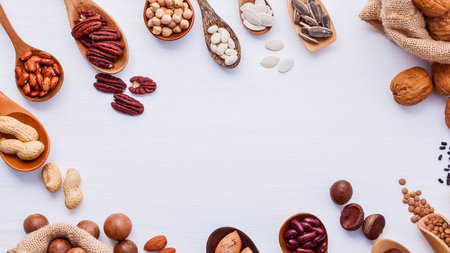A variety of nuts and seeds are artfully arranged in wooden spoons and scattered across a clean white surface, creating a delightful food composition.の写真素材