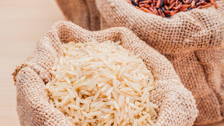 Close-up of hands cupping a generous portion of white rice, with burlap sacks and colorful grains visible.の写真素材