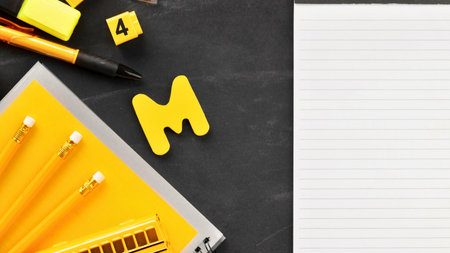 A flat lay of yellow school supplies including pencils, a marker, and alphabet blocks next to a blank sheet of lined paper.の写真素材