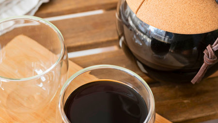 Close-up of two glasses with beverages and a dark coffee pot on a textured wooden surface.の写真素材