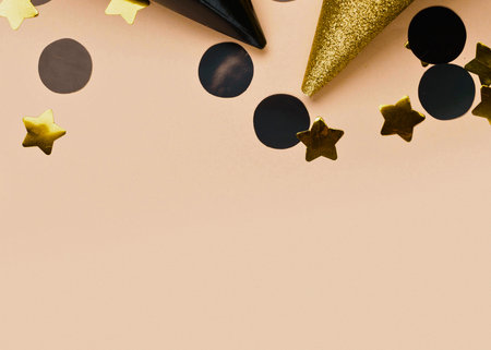 A top-down view of black and gold party hats with scattered black circles and gold stars confetti on a plain light background.の写真素材