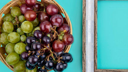 A close-up shot of a wicker basket overflowing with a variety of fresh green, red, and dark purple grapes.の写真素材