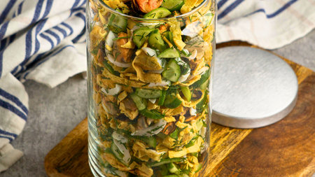 A tall glass jar filled with a vibrant, layered salad, showcasing fresh vegetables and greens, ready to be enjoyed.の写真素材