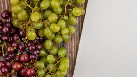 A close-up shot showcases bunches of vibrant green and deep red grapes resting on a rustic wooden background with a white space to the right.の写真素材