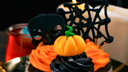 A festive Halloween cupcake adorned with a bright orange pumpkin and dark black frosting, set against a blurred background.の写真素材