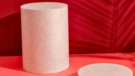 A tall, textured white cylinder stands against a vibrant red, leaf-patterned backdrop with a matching circular base nearby.の写真素材