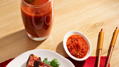 A vibrant spread featuring a spicy red sauce, a refreshing red beverage, and delectable food items, all set with chopsticks on a wooden surface.の写真素材