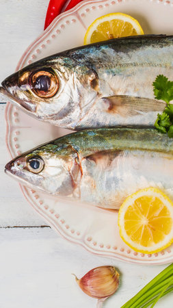 Two whole raw mackerel fish are presented on a plate with lemon slices, garlic, and herbs, ready for...