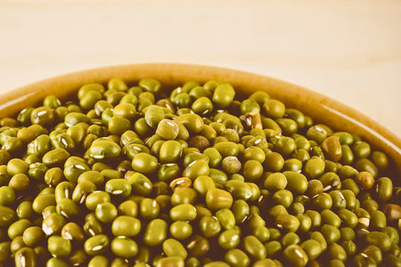 A detailed, close-up view of a bowl overflowing with small, round, green mung beans, showcasing their texture and color.の写真素材