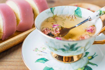 A delicate teacup with floral patterns holds a steaming herbal tea. Sliced bread rests on a golden tray in the background.の写真素材