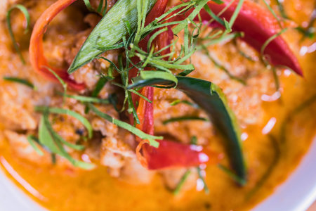 A close-up shot of a vibrant Thai red curry dish, garnished with fresh green herbs and red chili peppers, showcasing its rich texture and color.の写真素材